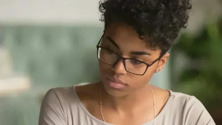 Woman with glasses and curly hair looking down thoughtfully, representing someone researching health information about HPV and immune support