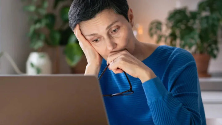 Person in a blue shirt looking thoughtfully at a laptop, representing health research of stress