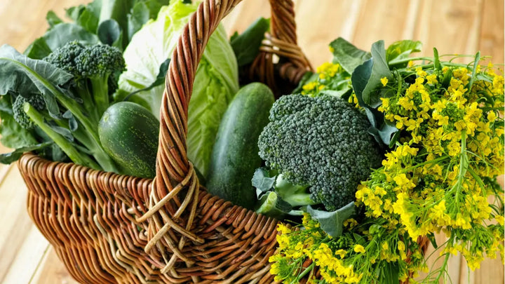 Wicker basket filled with fresh green vegetables including broccoli, spinach, and cucumbers