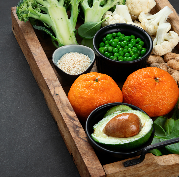 Wooden tray with nutrient-dense foods: broccoli, avocado, oranges, peas and mushrooms for immune health