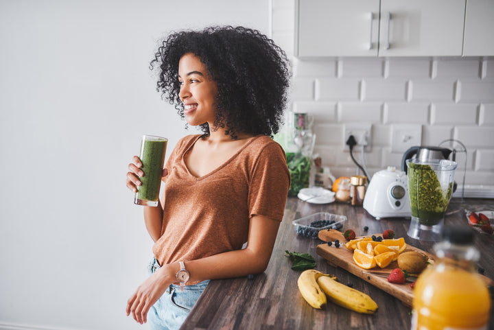 Smiling woman in kitchen holding a green smoothie, representing easy wellness habits